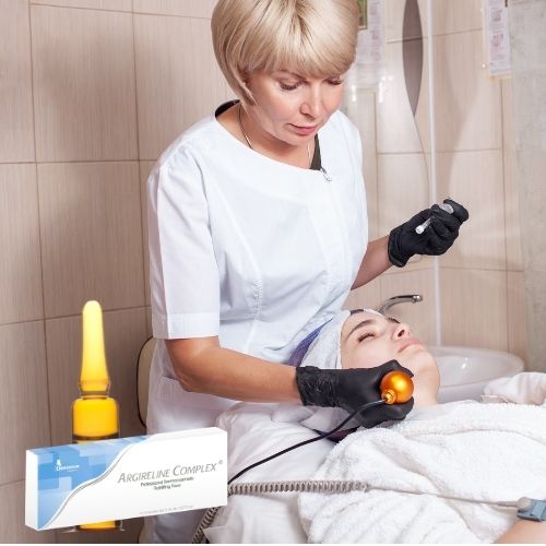 Esteticista haciendo tratamiento de electroporación en el rostro de mujer acostada.